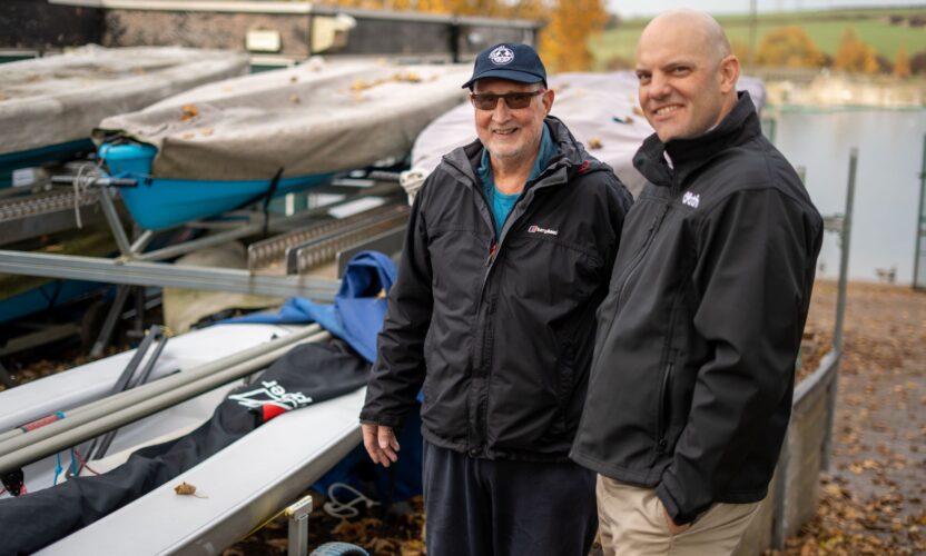 An image of commadore John from ulley Sailing club and Tom chaplin from onpath energy, standing next to some of the new boats Ulley sailing club has purchased with community fund grants